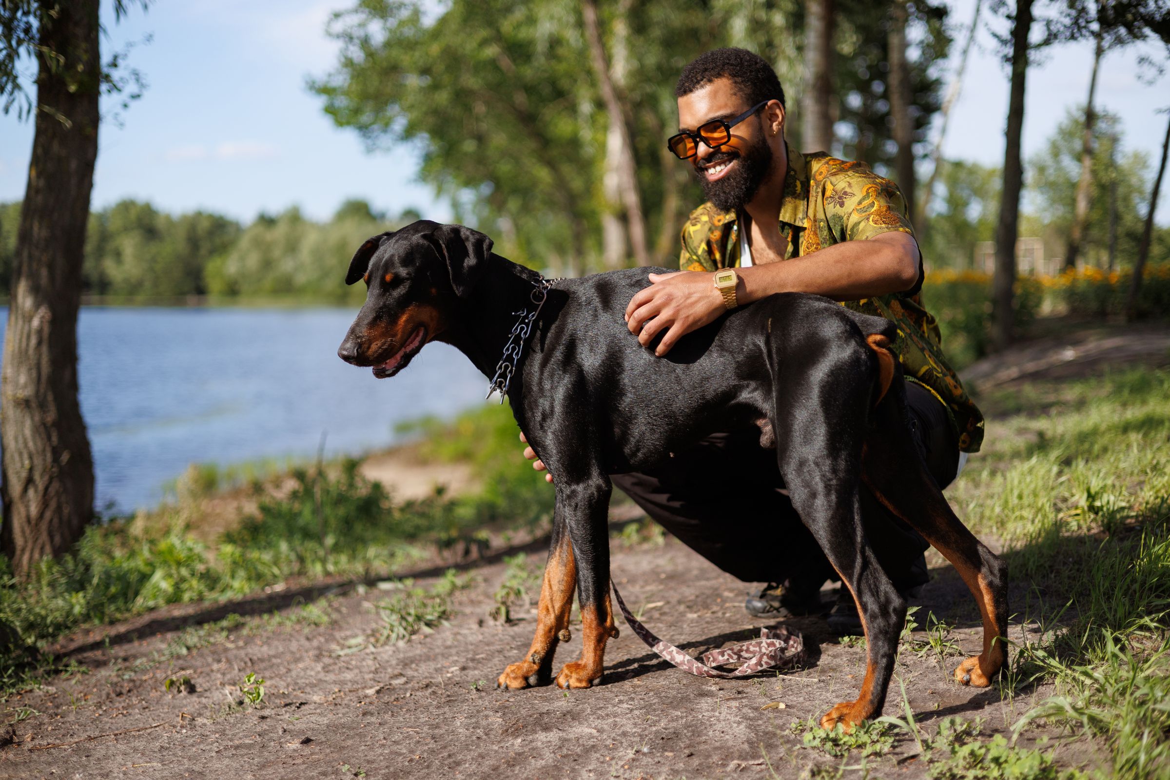 Smiling man hugging a Doberman dog near lake in park