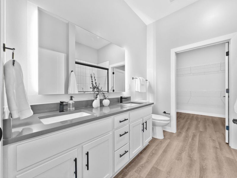 Modern bathroom at The Meridian with dual sinks, large mirror, and walk-in closet, featuring light-colored cabinetry and wood flooring