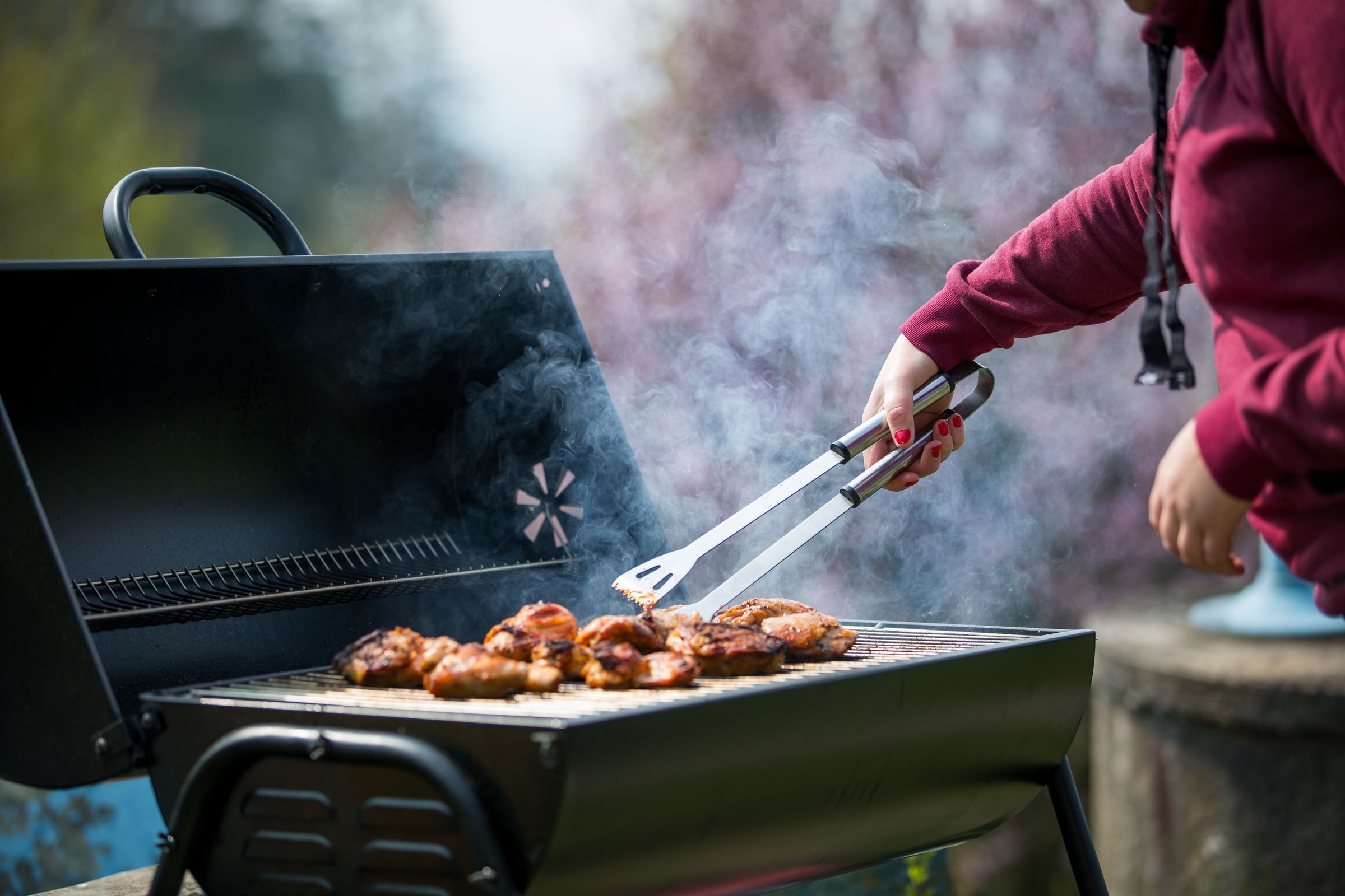 Young woman grills some kind of marinated meat and vegetable on gas grill during summer time