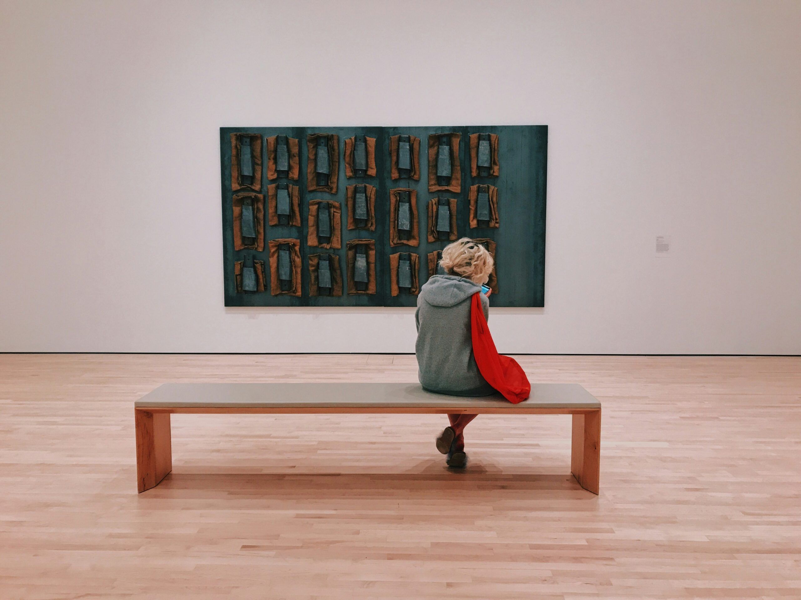 woman sitting on a bench looking at a pice of art on the wall